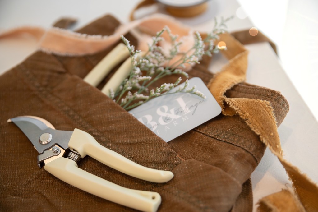 Floral apron, flower stems, ribbon, and Bloom & Forage business card arranged on a table
