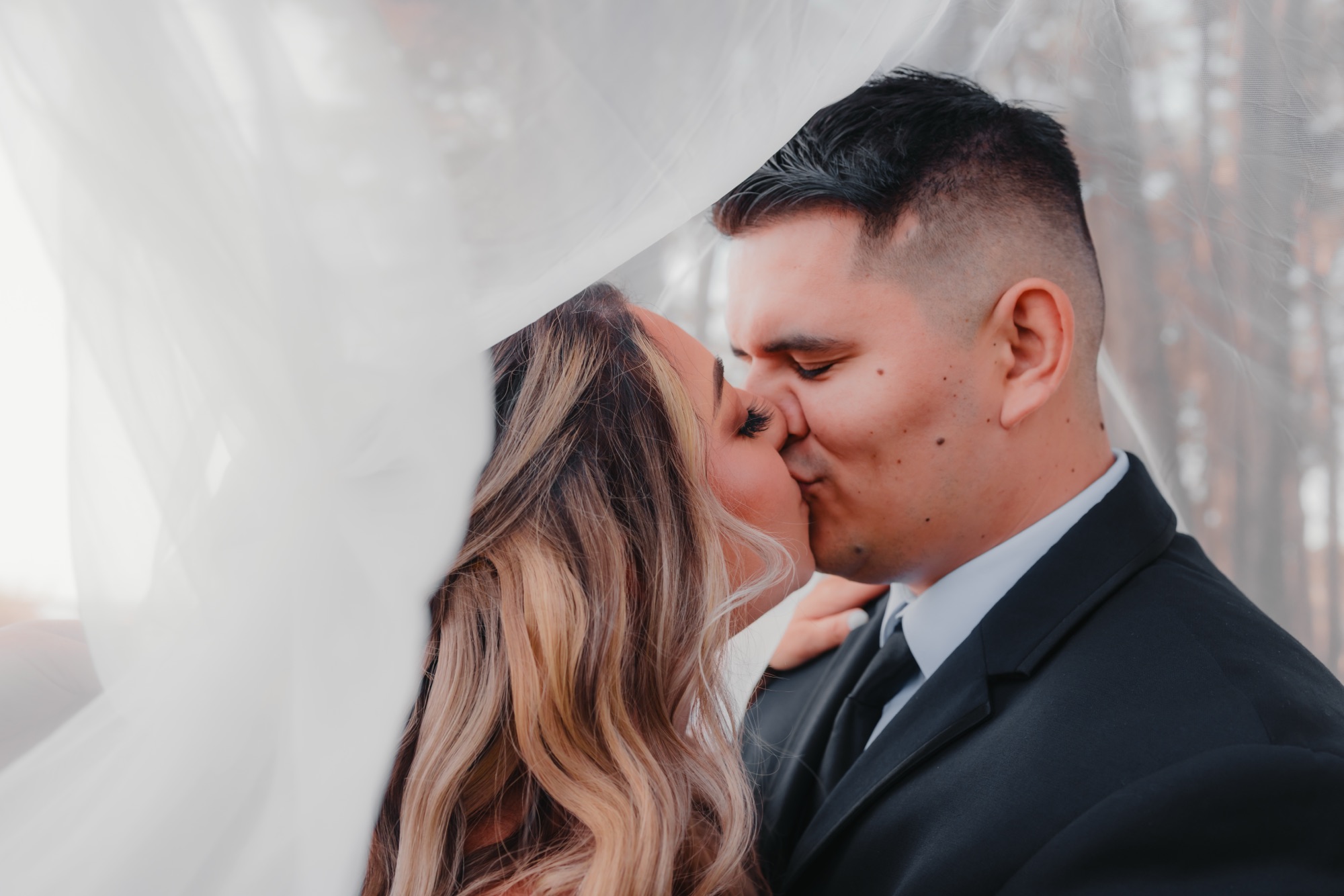 A bride and groom share a romantic kiss beneath the bride's veil on the bluff at Seascape Beach Resort in Aptos, California. Planned by Bloom & Forage with custom floral design, the moment captures the joy, intimacy, and natural beauty of their coastal wedding celebration.