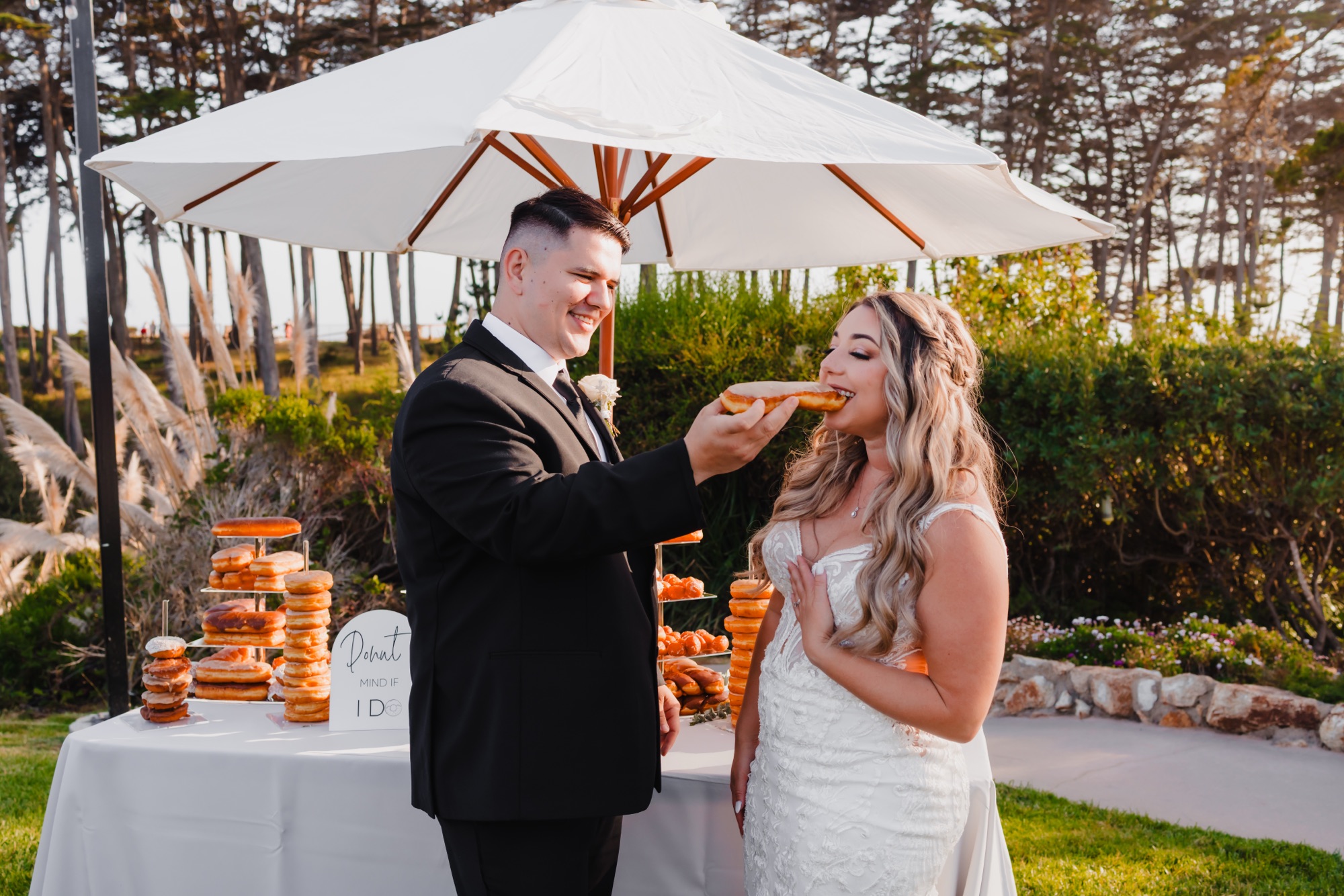 A bride and groom celebrate on the bluff at Seascape Beach Resort in Aptos, California, with a unique wedding donut display in place of a traditional wedding cake. Planned by Bloom & Forage, the celebration reflected the couple's personality while blending seamlessly with the romantic coastal setting.